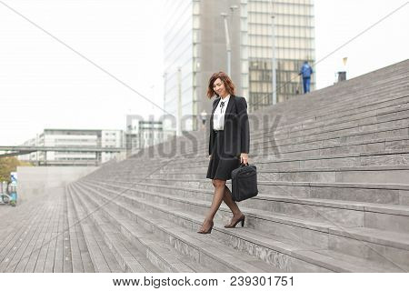 American Female Manager Going Down On Stairs In High Buildings Background. Concept Of Career And Bus