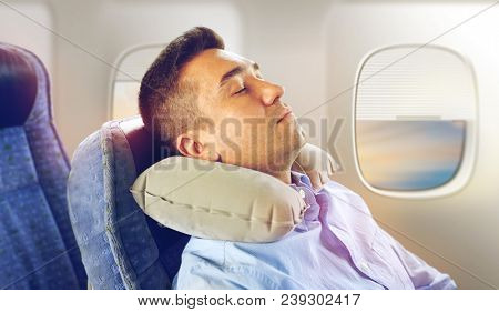 travel, comfort and people concept - man sleeping in plane with inflatable cervical neck pillow over porthole background