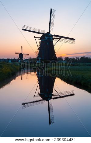 Sunrise With Traditional Dutch Windmills Reflected In The Calm Water Of The Canal.  Landscape With O
