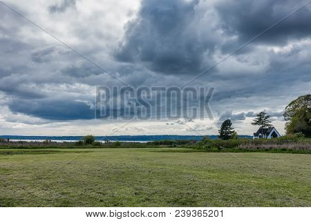 Dark Storm Clouds Hover Over A Green Meadow In Normany Park, Washington.