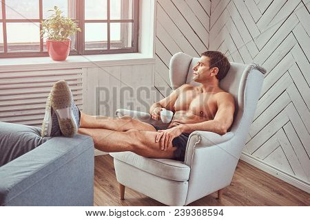 Handsome Shirtless Muscular Man Lying On The Chair, Drink Cup Of Tea, Resting After A Hard Workout A