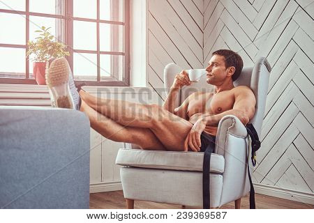 Handsome Shirtless Muscular Man Lying On The Chair, Drink Cup Of Tea, Resting After A Hard Workout A