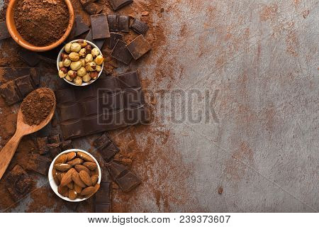 Dark Broken Chocolate Pieces On Dark Background, Cocoa Powder And Various Nuts In Bowls Closeup. Swe