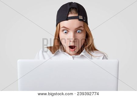 Surprised Female Looks With Bugged Eyes Into Screen Of Laptop Computer, Recieves Strange Unexpected 