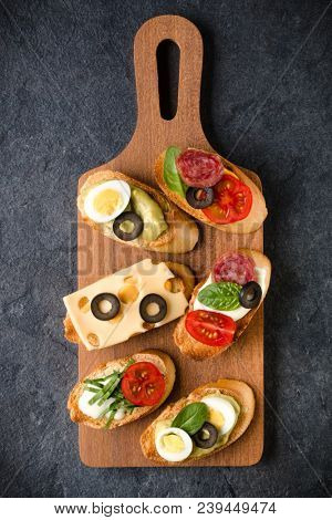 Open faced sandwich canape or crostini on a wooden serving board on dark stone  background closeup. Top view.