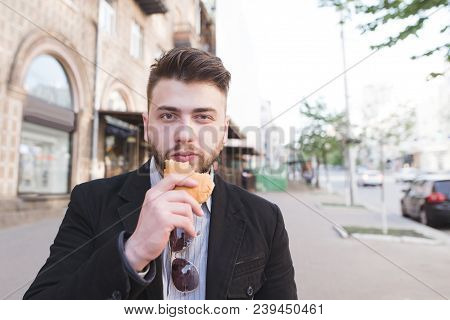Portrait Of A Bearded Man In A Suit With A Sandwich In The Hands Of A Street Background. A Busy Man 