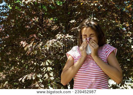 Young Girl With Allergy In Autumn Park. Sneezing Girl Blows Her Nose In A Napkin