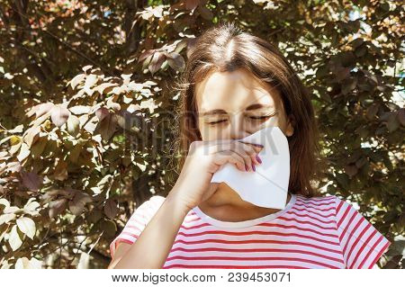 Young Girl With Allergy In Autumn Park. Sneezing Girl Blows Her Nose In A Napkin