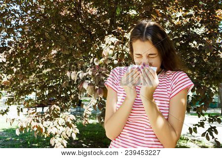 Allergy Concept. Sneezing Young Girl With Nose Wiper Among Blooming Trees In Park