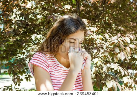 Allergy Concept. Sneezing Young Girl With Nose Wiper Among Blooming Trees In Park