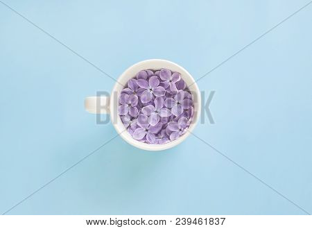 White Cup Full Of Lilac Flowers On The Blue Background.
