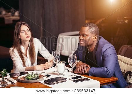 African Male In Blue Jacket Listens Attentively His Friend Sitting At Table Served For Dinner In Cos