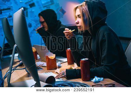 Female Hacker Working On Malware With Accomplice And Eating Junk Food