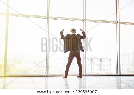 Excited Middle Age Businessman With Victory Reised Hands Up In Front Of Panoramic Window On Sunset