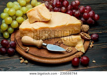Pieces Of Parmesan Or Parmigiano Hard Cheese And Grapes On Wooden Cutting Board