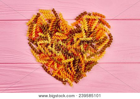 Shape Of Heart From Fusilli Pasta. Heart Made From Colorful Uncooked Fusilli Macaroni On Pink Wooden