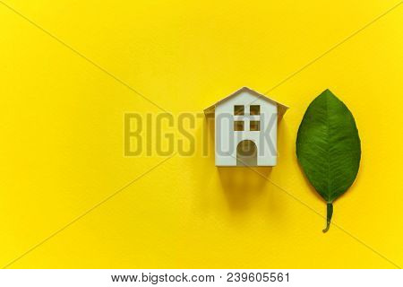 Miniature Toy Model House With Green Leaves On Yellow Colourful Trendy Backgdrop. Eco Village, Abstr