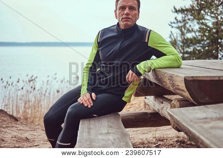 Jogger Sits On A Wooden Bench In The Woods, Resting After A Long Run.