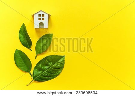 Miniature Toy Model House With Green Leaves On Yellow Colourful Trendy Backgdrop. Eco Village, Abstr
