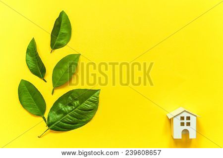 Miniature Toy Model House With Green Leaves On Yellow Colourful Trendy Backgdrop. Eco Village, Abstr