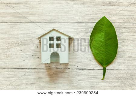 Miniature White Toy Model House With Green Leaves On Wooden Backgdrop. Eco Village, Abstract Environ