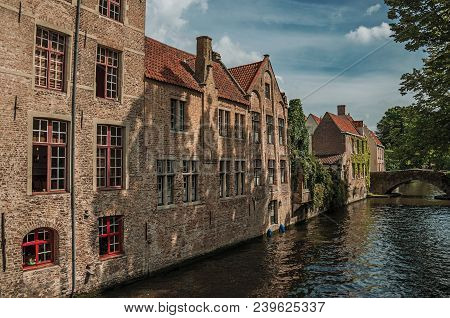 Wooded Gardens And Brick Buildings On The Canal Edge In A Sunny Day At Bruges. With Many Canals And 
