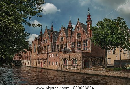 Wooded Gardens And Brick Buildings On The Canal Edge In A Sunny Day At Bruges. With Many Canals And 