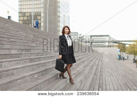 Pretty Businesswoman Going Down On Stairs In High Buildings Background. Concept Of Career And Busine