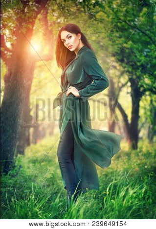 Beauty fashion model girl posing over blooming trees, enjoying nature in spring apple orchard. Beautiful brunette young woman over Garden with blooming apple trees. Outdoor full length portrait