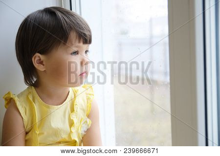 Little Girl Looking Out The Window Longing For Some Sunshine. Curiosity Childness. Child Sitting Hom