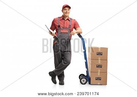 Full length portrait of a mover with a clipboard leaning on a hand truck with a stack of boxes isolated on white background