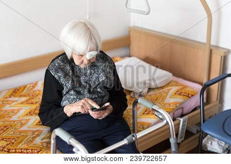 Lonley Elderly 95 Years Old Woman Sitting At The Bad Using Modern Mobile Phone Application To Monito