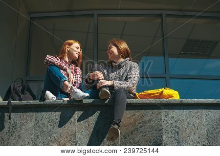 College Students Take A Break After Classes. Young Reddish Natural Girls Sit Outside Modern Building