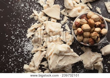 White Broken Chocolate Pieces On Dark Background, Coconut Powder And Hezelnuts In Bowl, Closeup. Swe