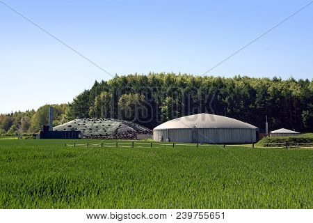 Biogas Plant For Renewable Energy In A Field In Front Of A Forest, Blue Sky, Copy Space, Selected Fo