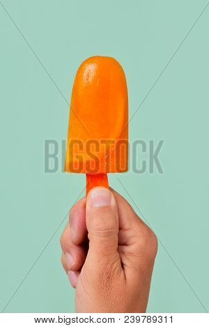 closeup of a young caucasian man with a homemade natural ice pop in his hand, against a green background