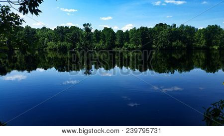 A Calm River Gives A Beautiful Reflection Of The Tree Line And Partially Cloudy Sky.