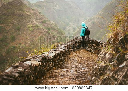 Hiker With Backpack On The Mountain Edge Cobbled Path Looking Down The Valley. Rocky Terrain Of High