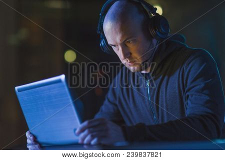 cybercrime, hacking and technology concept - male hacker with headset using laptop computer for cyber attack or wiretapping in dark room