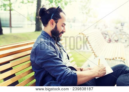 lifestyle, creativity, freelance, inspiration and people concept - creative man with notebook or diary writing sitting on city street bench