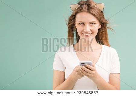 Happy Smiling Blonde Teen Girl Holds Smartphone On Blue Background
