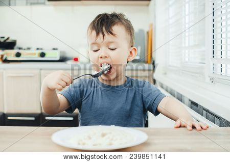The Little Boy In The Kitchen Eagerly Eating Rice With A Spoon Independently