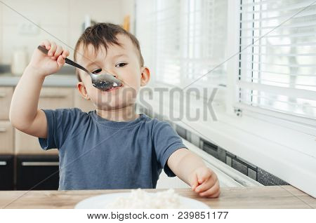 The Little Boy In The Kitchen Eagerly Eating Rice With A Spoon Independently