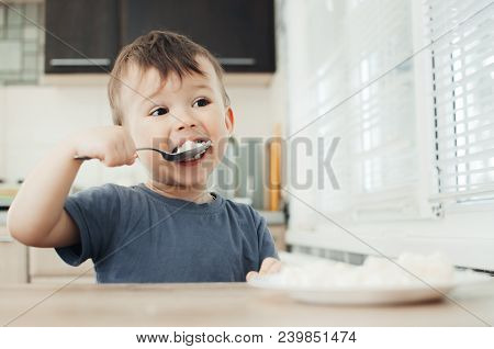 The Little Boy In The Kitchen Eagerly Eating Rice With A Spoon Independently