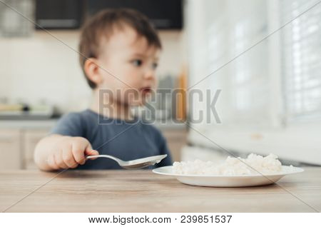 The Little Boy In The Kitchen Eagerly Eating Rice With A Spoon Independently
