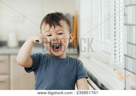 The Little Boy In The Kitchen Eagerly Eating Rice With A Spoon Independently