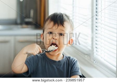 The Little Boy In The Kitchen Eagerly Eating Rice With A Spoon Independently