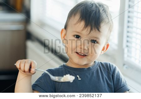 The Little Boy In The Kitchen Eagerly Eating Rice With A Spoon Independently