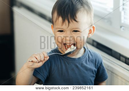 The Little Boy In The Kitchen Eagerly Eating Rice With A Spoon Independently