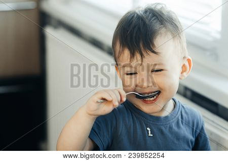 The Little Boy In The Kitchen Eagerly Eating Rice With A Spoon Independently